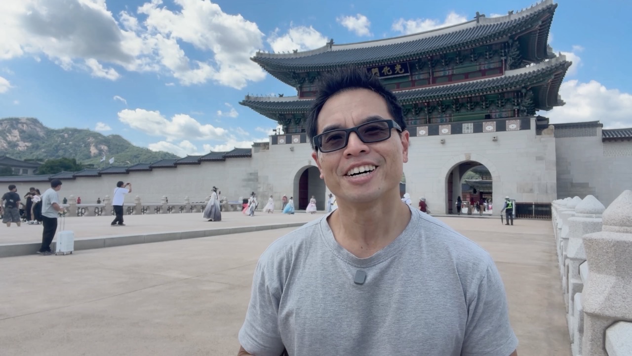 Dr Derrick Siu, smiling to camera at Gwanghwamun Gate in Seoul